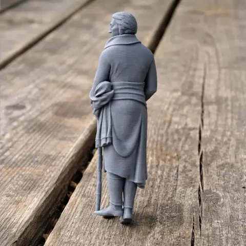 3D-printed figure of a historical warrior in a long coat, holding a hat and cane, on a wooden surface.