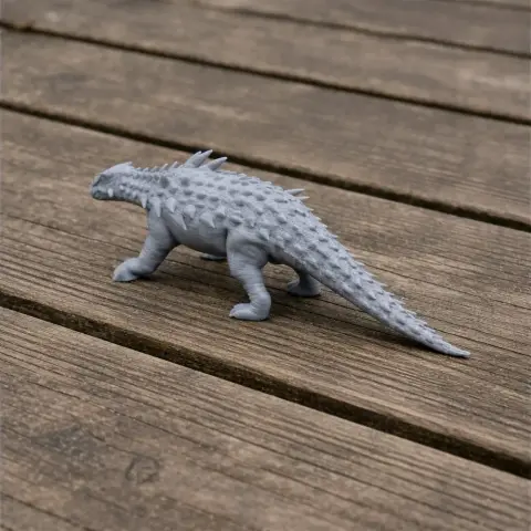 Gray 3D-printed Polacanthus model on a wooden surface, showcasing spiky armor and a long tail.