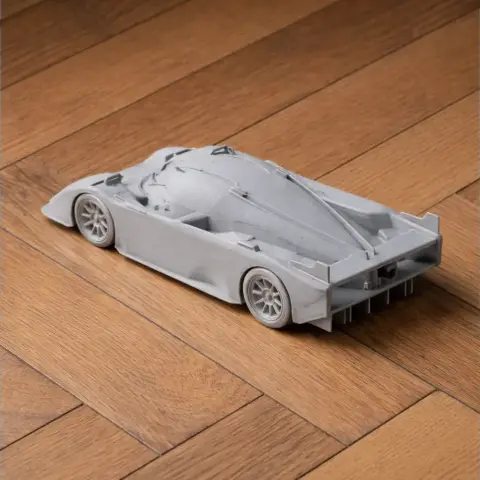 Gray scale model of a sleek sports car with aerodynamic design on a wooden floor.