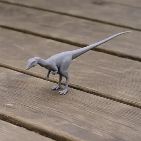A small, gray 3D-printed dinosaur model with a long tail on a wooden surface.