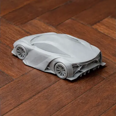A sleek, futuristic scale model car, 3D printed in gray, on a wooden floor.