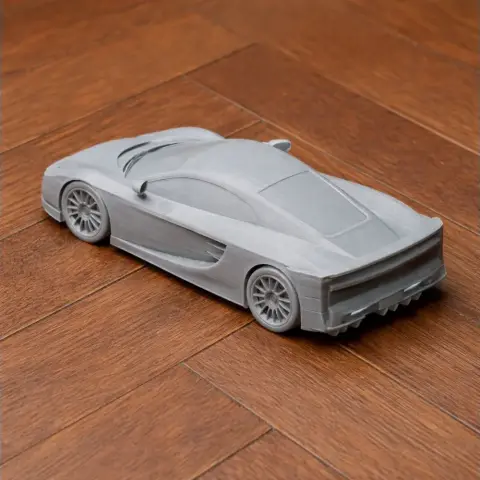Gray 3D-printed model of a sleek, aerodynamic sports car on a wooden surface.