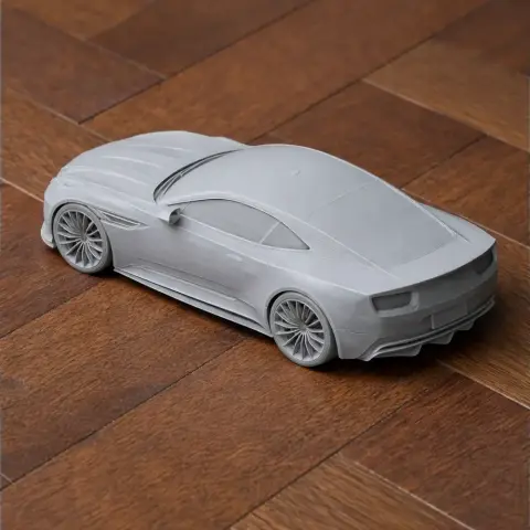 3D printed gray model of an Aston Martin DB12, detailed on a wooden surface.