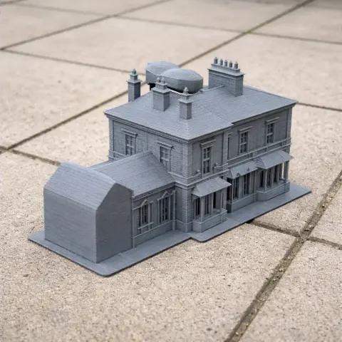 Gray 3D-printed model of a detailed, old-style building with chimneys, placed on a tiled surface.