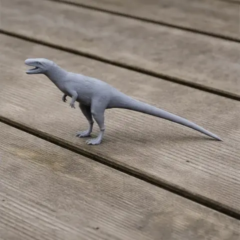 Gray 3D-printed Sinosauropteryx model with open mouth, posed on a wooden surface.