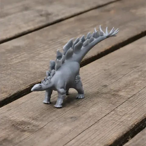 Gray 3D-printed Stegosaurus model on a wooden surface, featuring distinctive back plates and tail spikes.