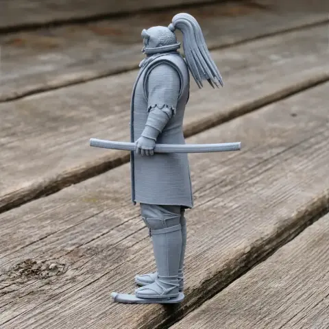 3D printed samurai figure with ponytail, armor, and a sheathed sword, standing on wooden surface.