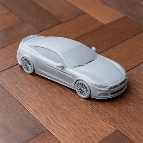 A sleek, gray 3D-printed model of an Aston Martin Rapide on a wooden surface.