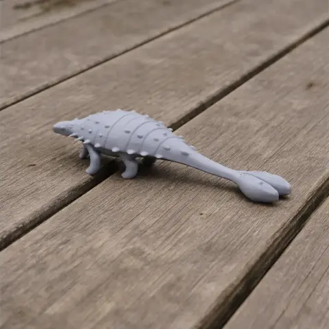 A small 3D-printed model of a Tarchia dinosaur with a spiked tail and armored body on a wooden surface.
