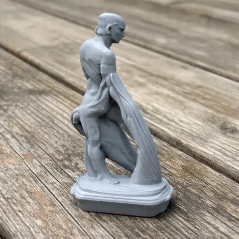 3D-printed ancient warrior statue, muscular figure in draped cloth on a wooden surface.