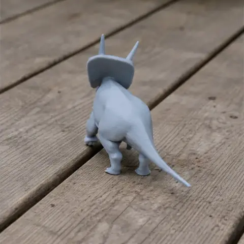 A 3D printed model of a Torosaurus, viewed from behind, standing on wooden planks.