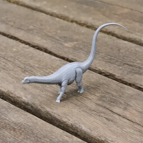 Gray 3D-printed model of a long-necked dinosaur with a long tail on a wooden surface.