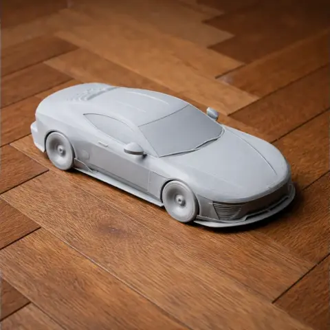 3D-printed model of a sleek sports car on a wooden floor, showcasing detailed bodywork.
