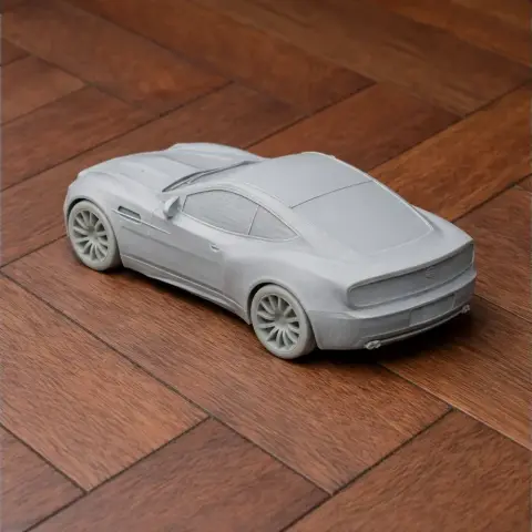 3D printed model of an Aston Martin Vanquish, unpainted, on a wooden surface.