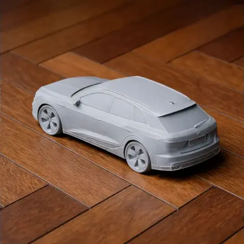 A scale model of a sleek, futuristic car, 3D-printed in gray, placed on a wooden floor.