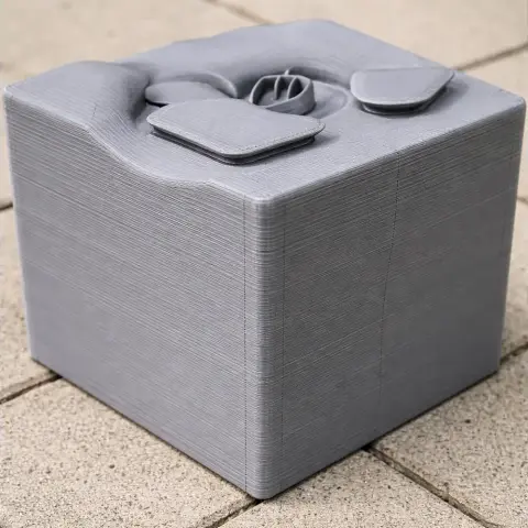 A 3D-printed gray cube with abstract, layered top architecture.