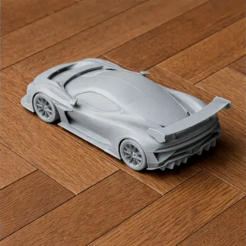 Gray 3D-printed model of an Aston Martin Vulcan, showcasing its sleek design, on a wooden surface.