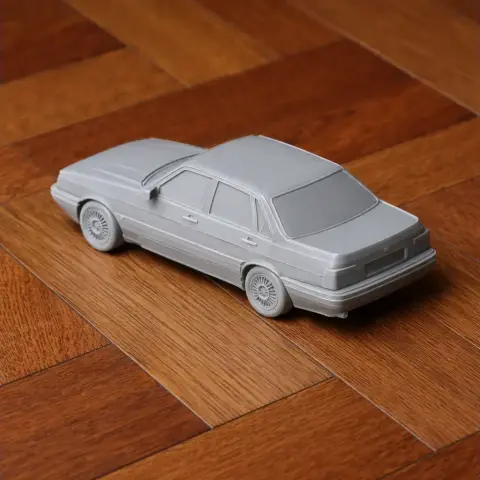 3D printed model of an Audi 90 car on a wooden surface, showcasing detailed wheels and body.