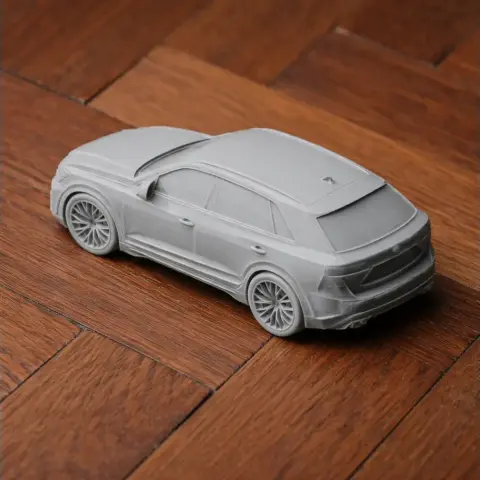 3D-printed model of an Audi Q8, gray, detailed, on a wooden surface.