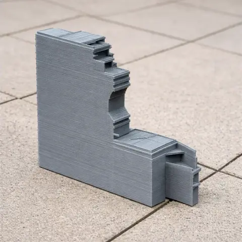 3D-printed gray architectural model with stair-step design on tiled surface.
