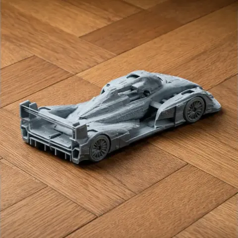 Model of a detailed Audi R15 TDI race car, 3D printed in gray, shown on a wooden surface.