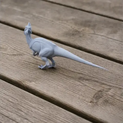 A small, gray 3D printed dinosaur model with a long tail on a wooden surface.