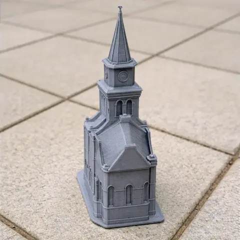 3D printed model of a Protestant church with a tall spire, placed on a tiled surface.