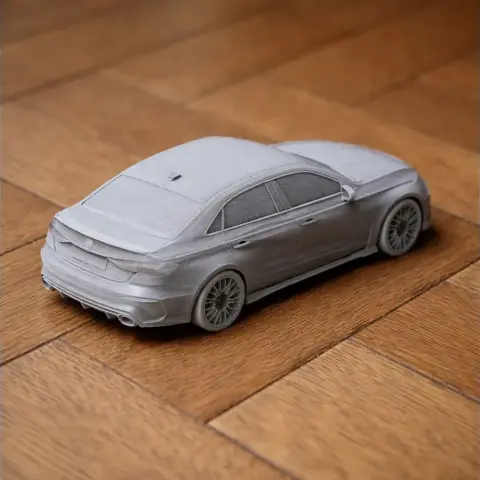 Gray 3D printed model of an Audi RS3 car on a wooden surface.