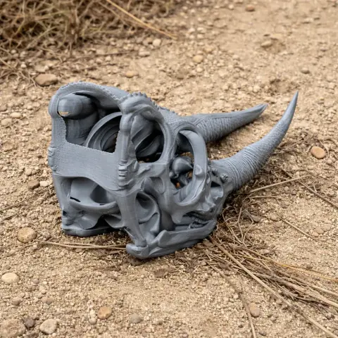 3D printed Jackson's chameleon skull replica with prominent horns, displayed on rough ground.