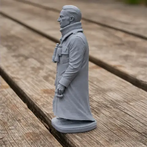 3D model of a WWII soldier in a long coat, holding binoculars, on a wooden surface.
