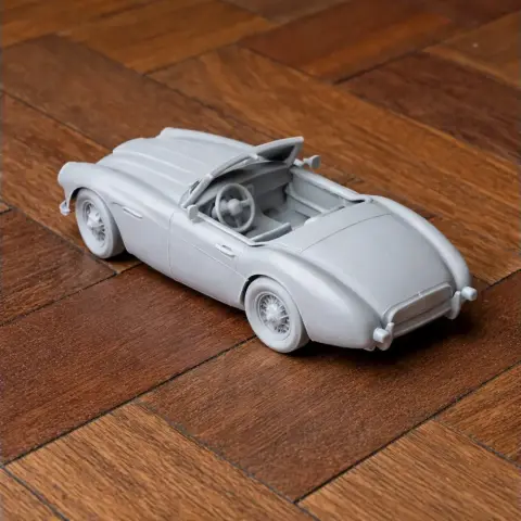 3D printed model of an Austin-Healey 100 car, placed on a wooden surface.