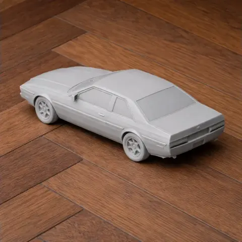 3D printed model of a classic car on a wooden floor, featuring detailed wheels and smooth body design.