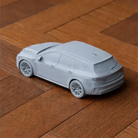 A 3D-printed scale model of a BMW iX car in gray, displayed on a wooden surface.