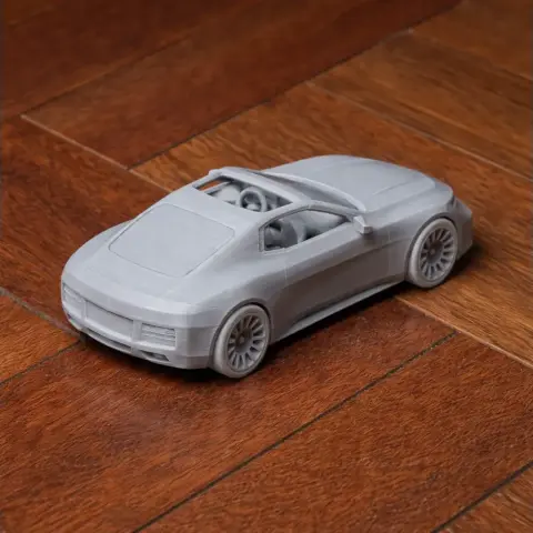 3D-printed scale model of a sleek, modern car with an open roof, placed on wooden flooring.