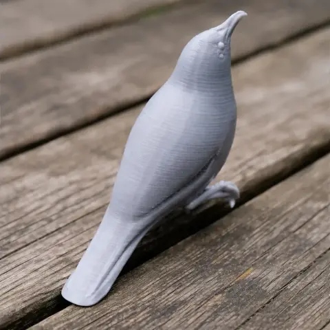 A gray 3D-printed model of a bird standing on a wooden surface.