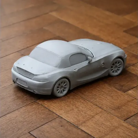 3D printed model of a BMW Z4 car in gray, on a wooden surface.