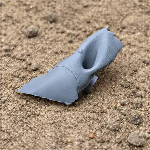 A gray 3D-printed Avaceratops skull replica on sand.