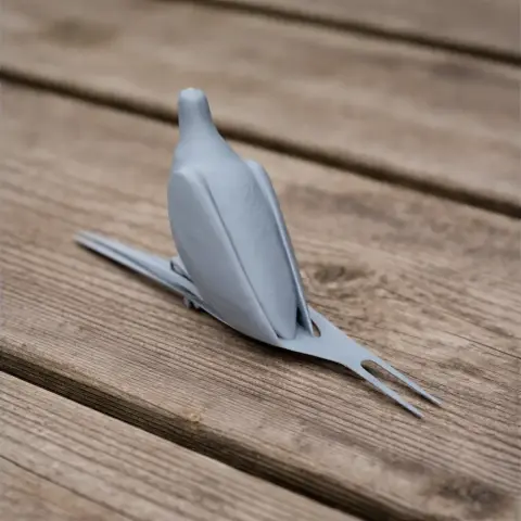3D printed model of a sleek, stylized pigeon perched on a branch, shown on a wooden surface.