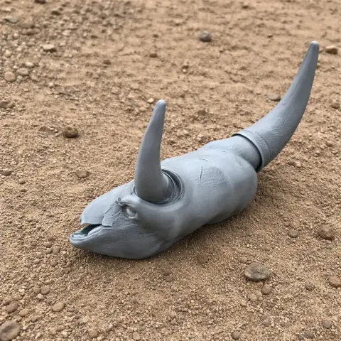 Gray, horned, dinosaur-like skull model on sandy ground.