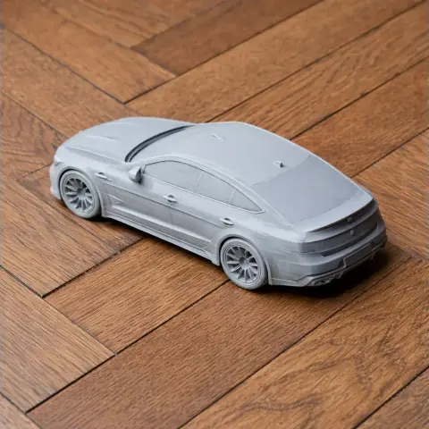 Gray 3D-printed model of a sleek sportscar with detailed wheels, displayed on wooden flooring.