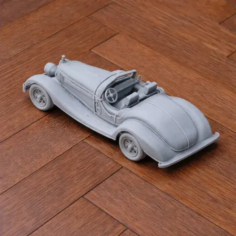 Gray scale model of a vintage convertible car on a wooden surface.