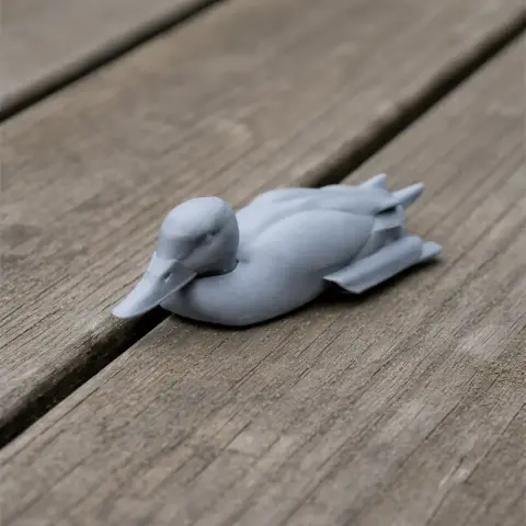 3D printed gray model of a duck-like bird resting on a wooden surface.
