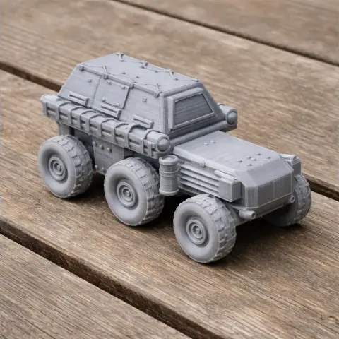 Gray 3D-printed six-wheeled vehicle model with an armored design on a wooden surface.