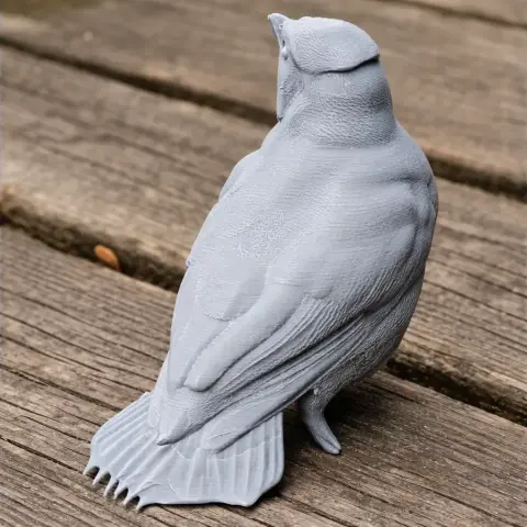 Gray 3D-printed bird figure with detailed feathers, perched on a wooden surface.