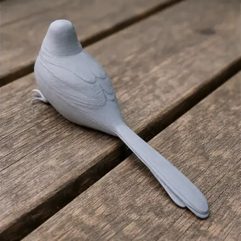 3D-printed model of a bird with detailed feathers, perched on a wooden surface.