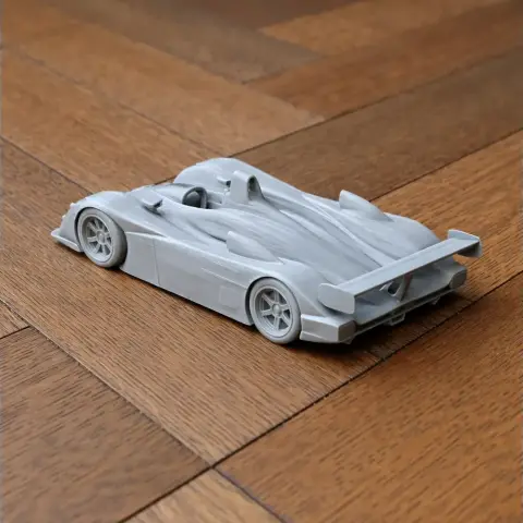 3D-printed model of a sleek race car with detailed curves and a rear spoiler on wooden surface.