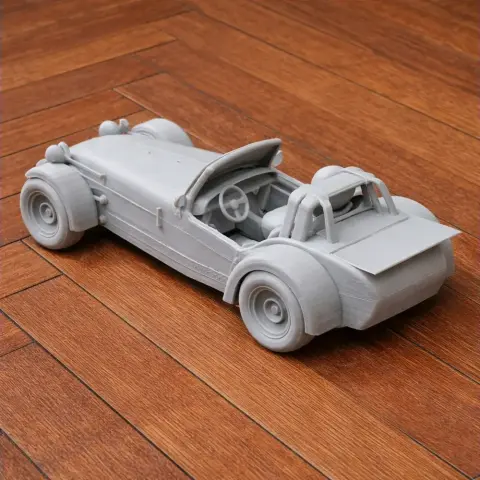 3D-printed model of a Caterham Seven, a detailed open-top sports car, on a wooden surface.
