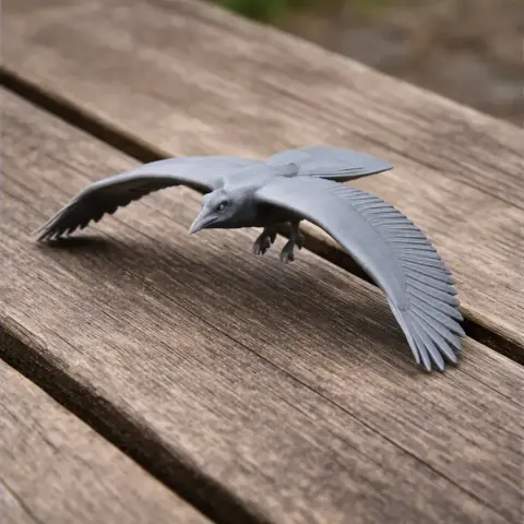 Gray 3D-printed model of a magpie with outstretched wings, displayed on a wooden surface.
