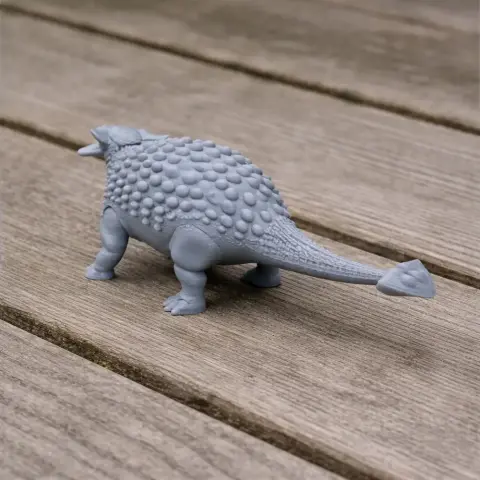 Gray 3D printed dinosaur model with textured back and long tail on wooden surface.