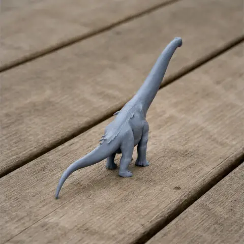 Gray 3D-printed Adamantisaurus figurine on a wooden surface, showcasing a long neck and tail.